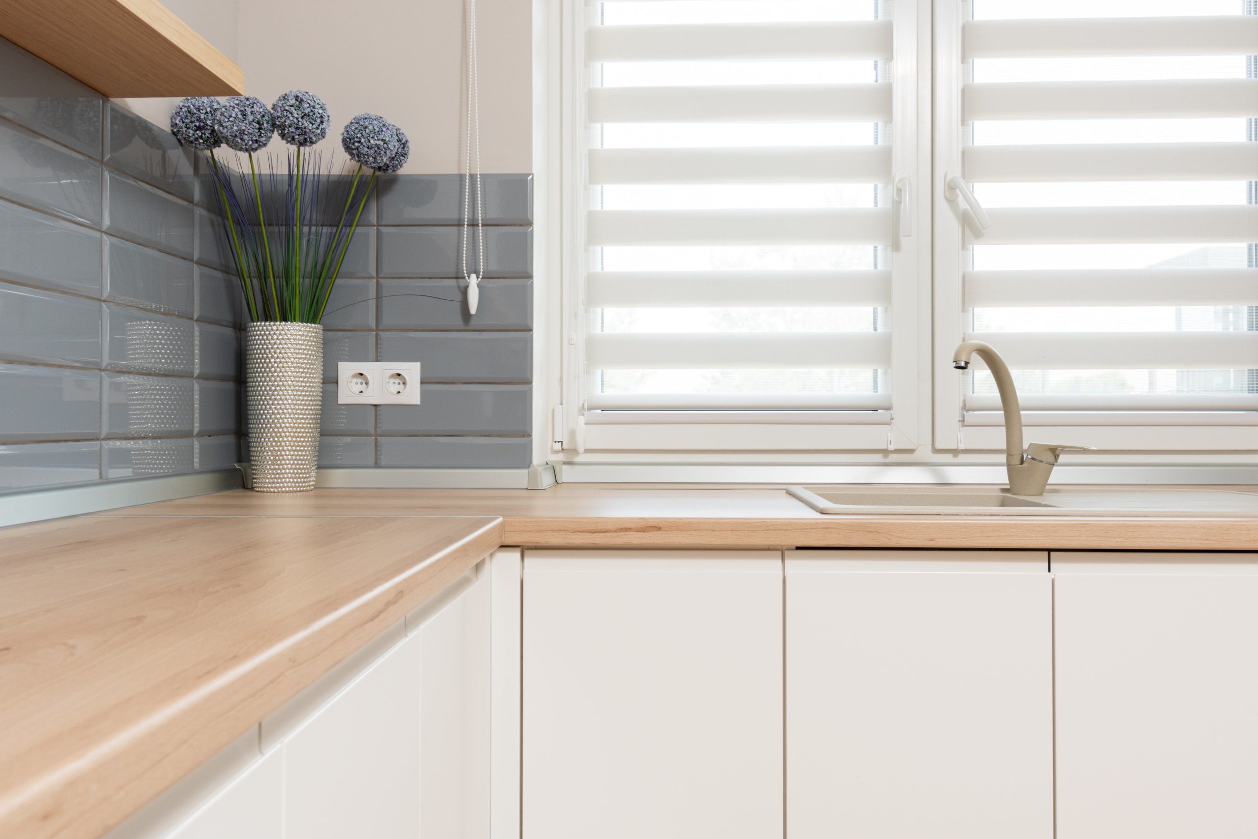 wide view of a clean kitchen counter top with a vase of tulips and a window with light coming through the blinds